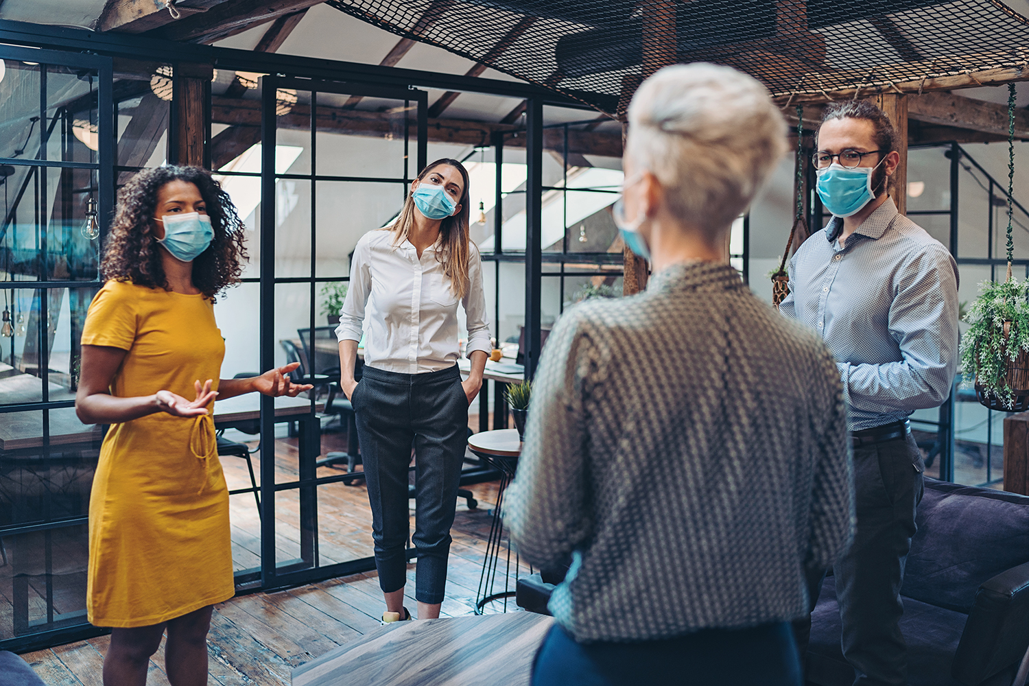 A group of people wearing blue masks in an office space. They are practicing social distancing.