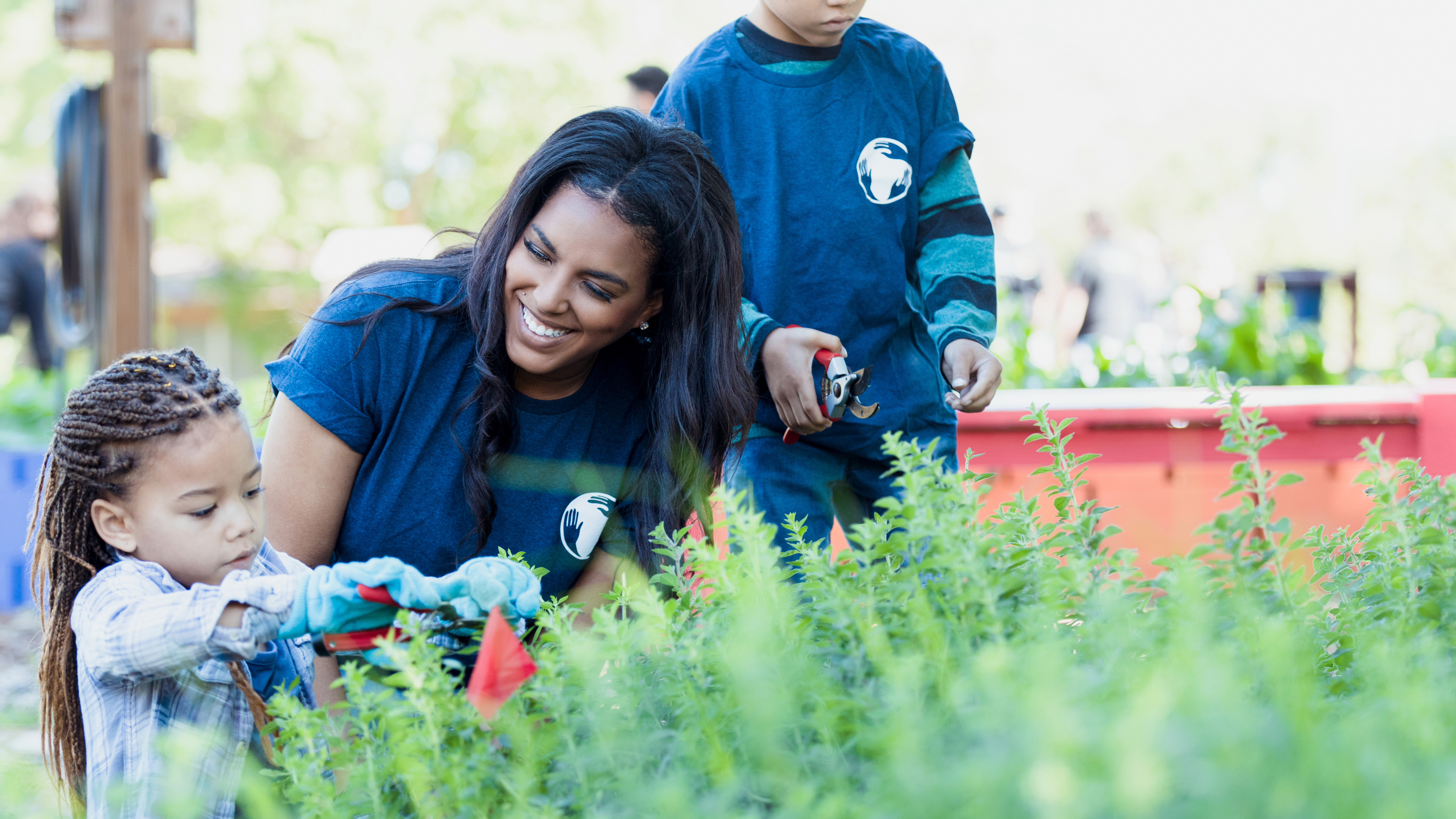 Smiling woman and little girl are gardening with a little boy standing behind them.