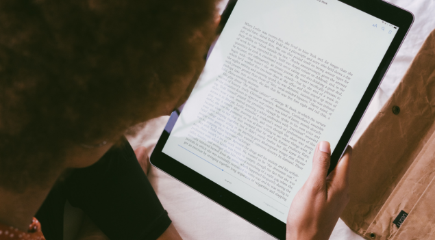 A woman reads a page of text from a e-reader app on a tablet.