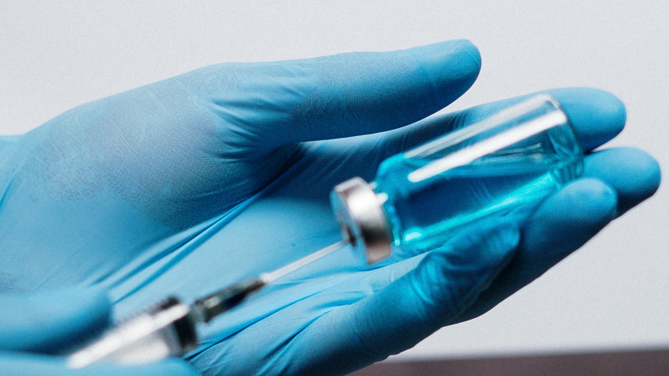 Person's hands in blue gloves prepares a vaccination with a syringe and a small bottle.