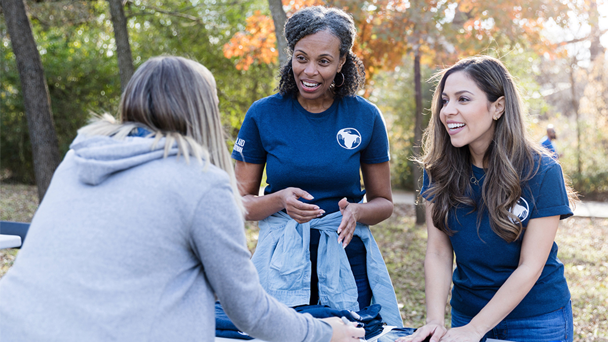 Two women who work at a registration table talking with a volunteer during a community event.