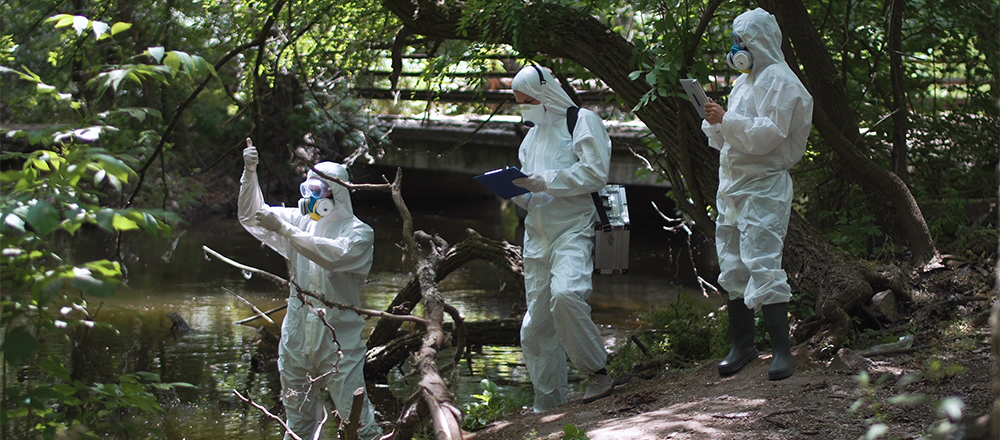 People in white protective gear examine water from a river.