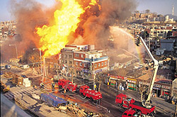 Aerial view of a building in a city on fire with firetrucks putting out the fire.