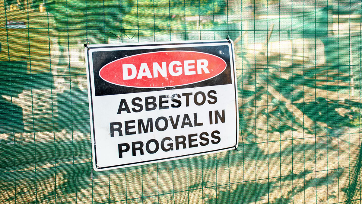 A warning sign Danger Asbestos on a fence at construction site where old house is demolishing