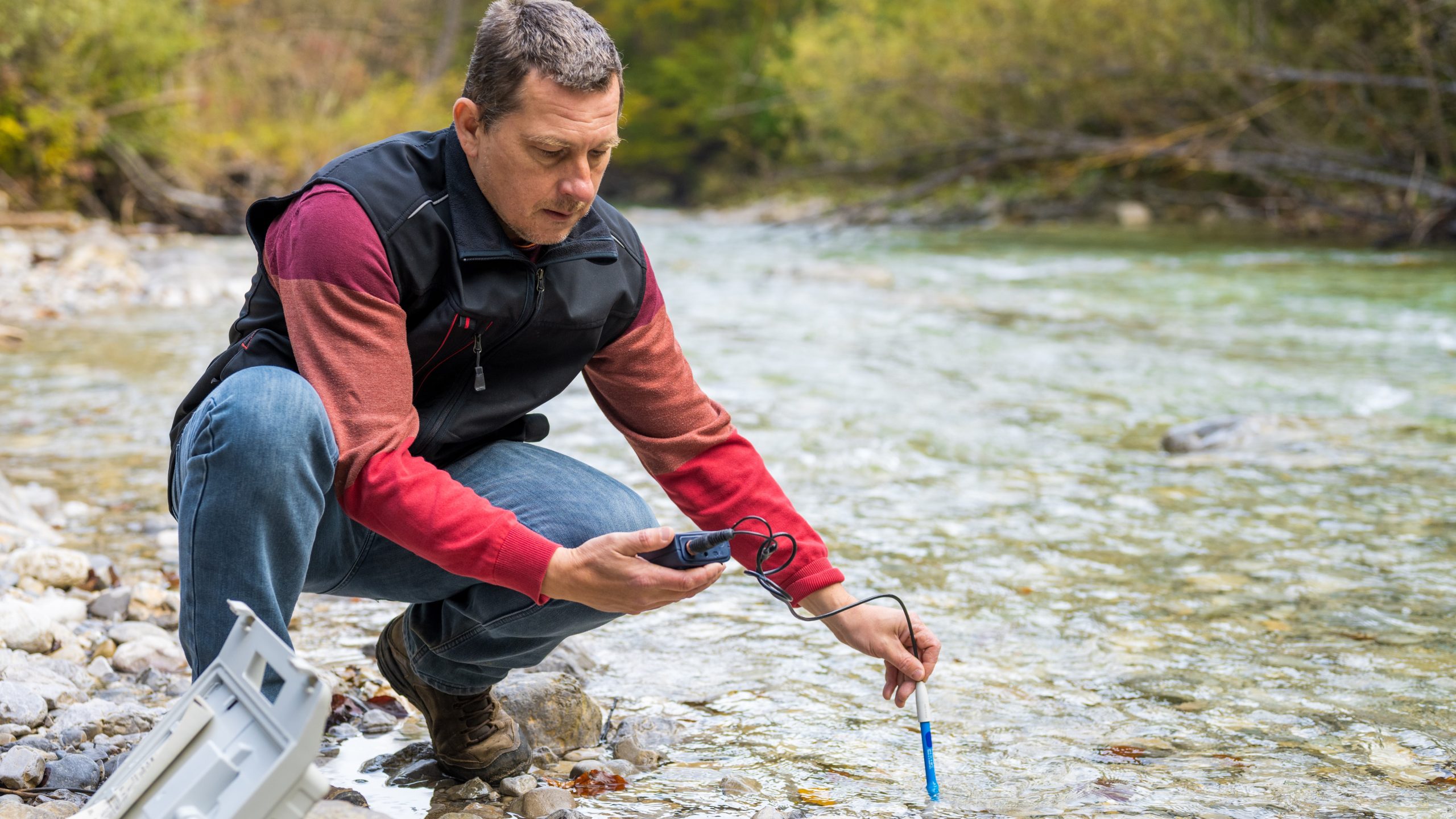 Man analyzing quality of water in river using electronic measuring equipment to reveal water pollution