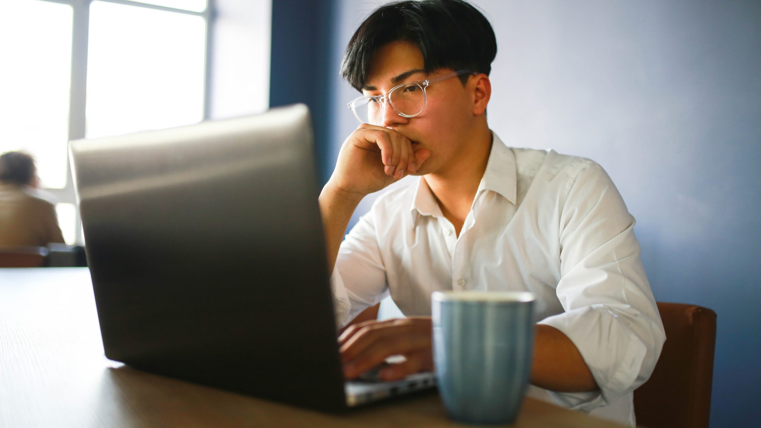 Young man working hybrid remotely from laptop in cafe