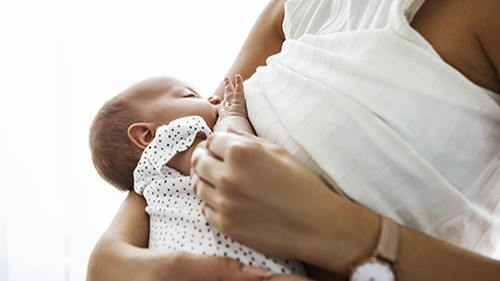 Mother breastfeeding and holding newborn baby