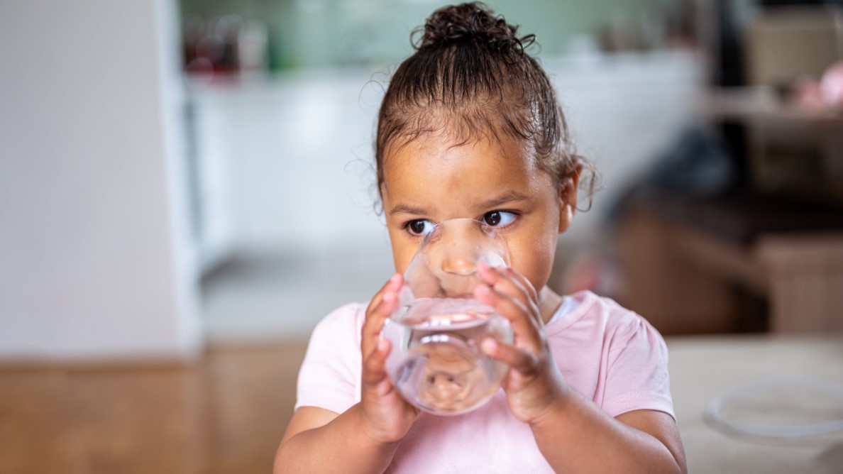 A small child with a pink shirt drinking water out of a glass.