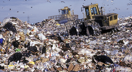 Bulldozers moving large piles of trash around a landfill.