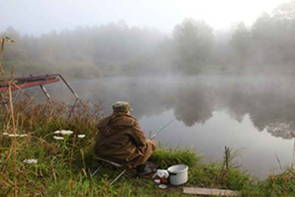 Man sitting on the side of a river while fishing