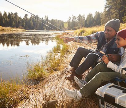 Grandfather teaching grandson to fish at local lake.