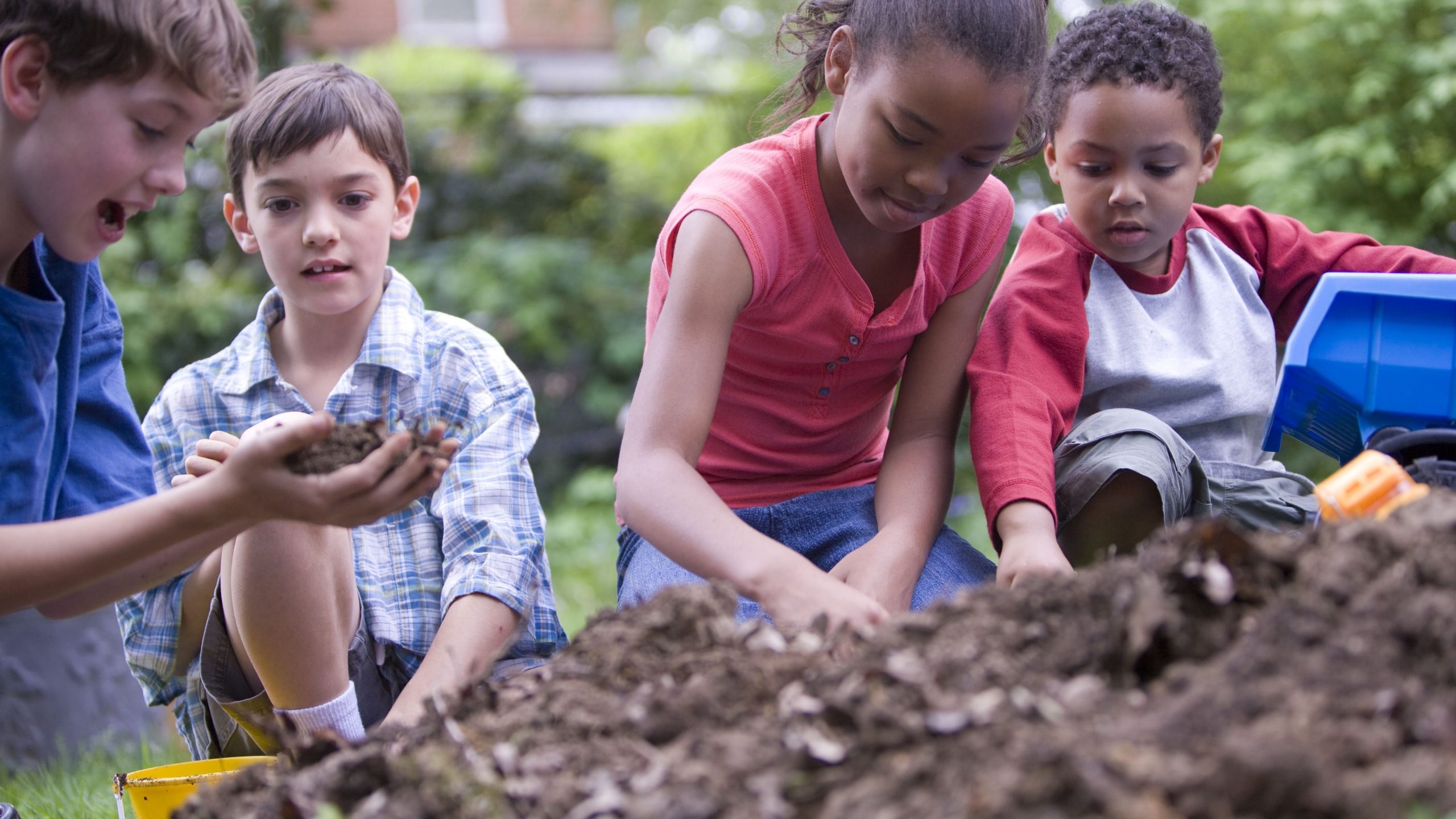 Four young children playing outside in a backyard dirt pile