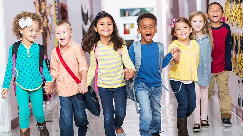 Multiracial group of preschoolers running down hallway